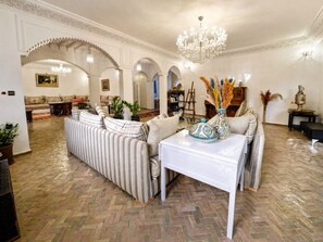 A spacious living room with a herringbone floor, striped sofas, a white coffee table, and a chandelier.