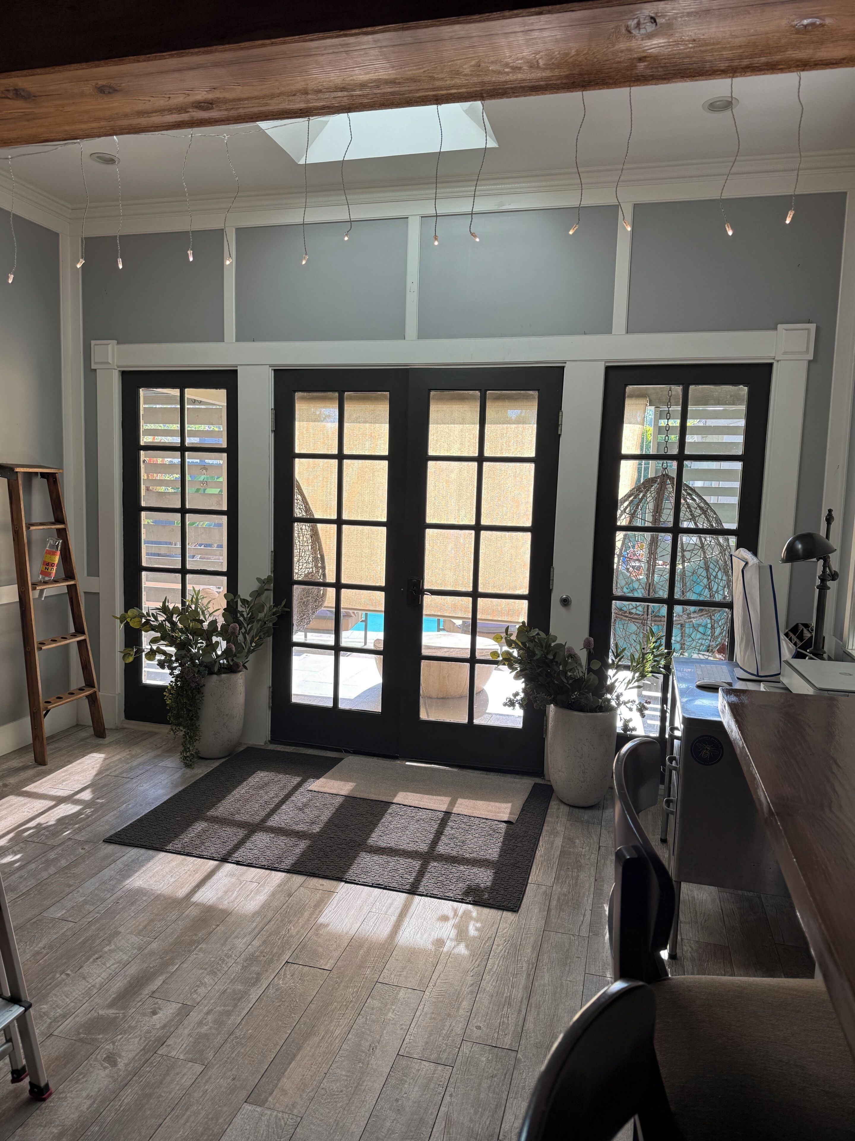 Habitación con escritorio, computadora y plantas en macetas. Se observan dos puertas con ventanas, una escalera y una claraboya.