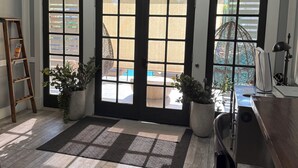 Ein Zimmer mit Schreibtisch, Computer und Topfpflanzen. Zwei Türen mit Fenstern, eine Leiter und ein Oberlicht sind vorhanden.