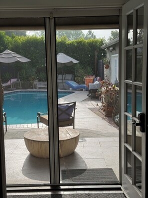 Ein Poolbereich mit rundem Tisch und Stühlen, Sonnenschirmen und Pflanzen in Töpfen.