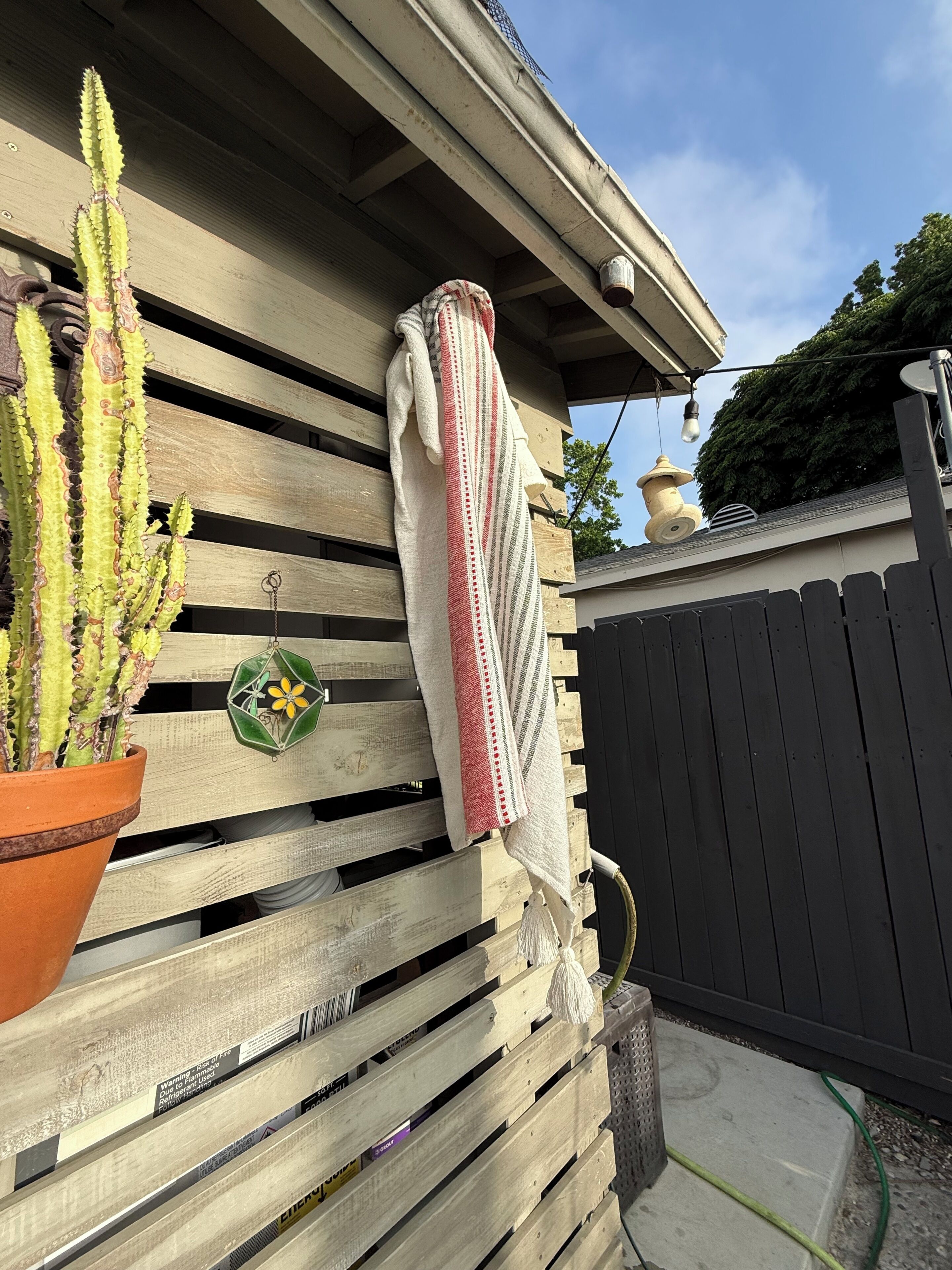 A wooden slatted wall with a potted cactus, a hanging towel, and a small decorative item.