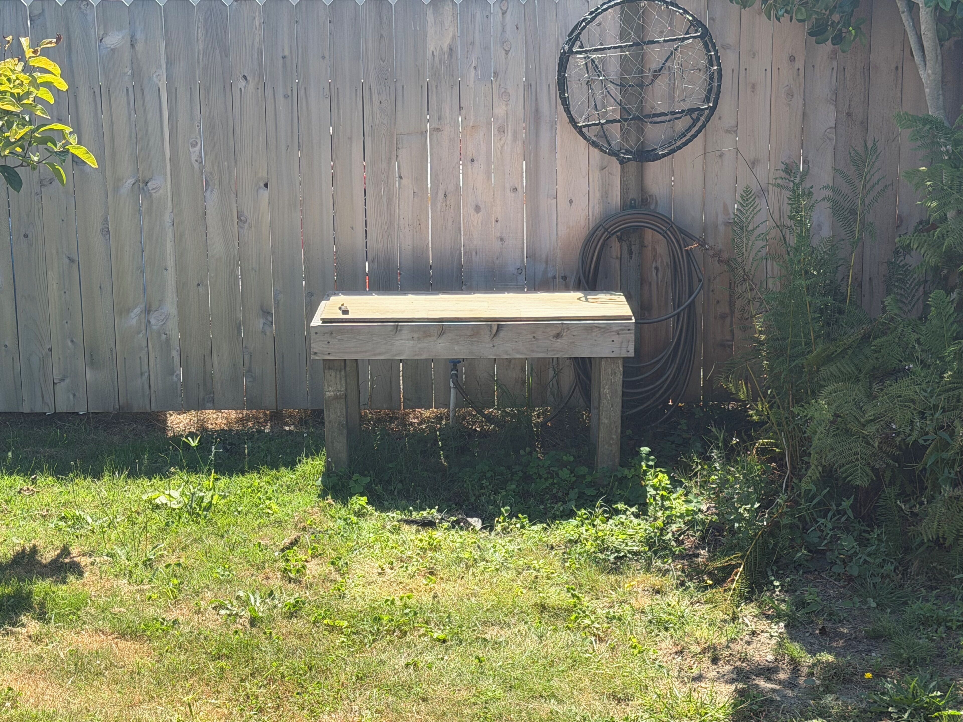 A wooden bench in a garden with a wooden fence and a garden hose in the background.