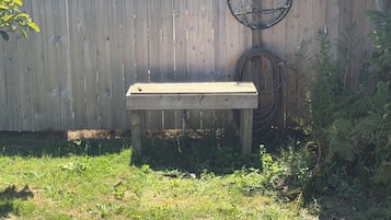 A wooden bench in a garden with a wooden fence and a garden hose in the background.