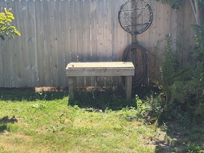 Una panchina di legno in un giardino con una recinzione di legno e un tubo da giardino sullo sfondo.