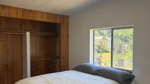 A bedroom with a bed, a wooden wardrobe, a window with a view, and a ceiling light.