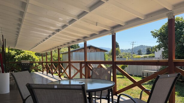 An outdoor patio with a table and chairs, a grill, and a view of a house and trees.