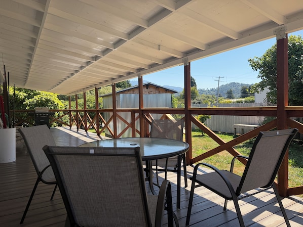 An outdoor patio with a table and chairs, a grill, and a view of a house and trees.