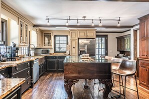 A spacious kitchen with a central island, dark wood cabinetry, and a stainless steel refrigerator. - The Midland Clubhouse - Pool and Golf Simulator! (Pinehurst)