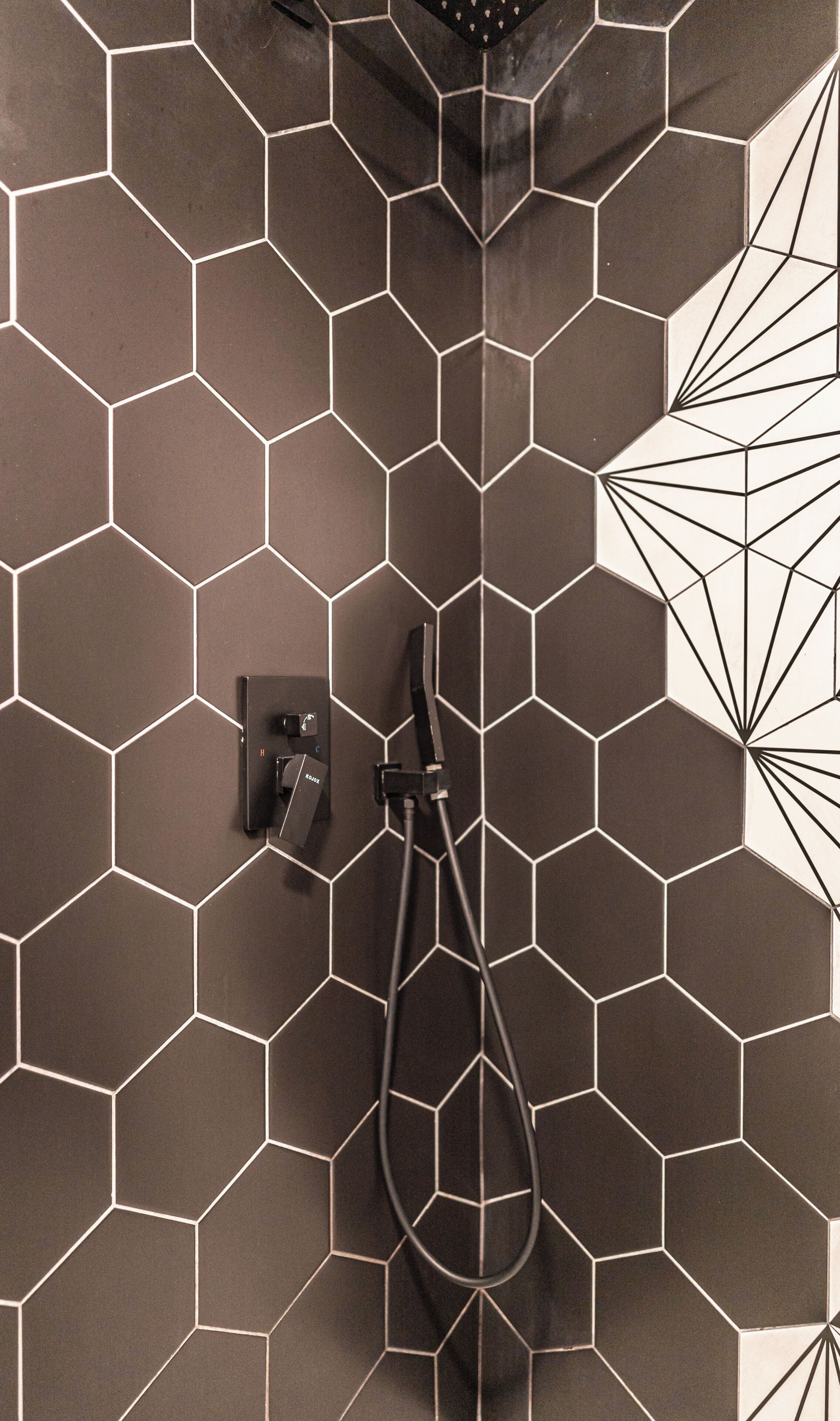 A bathroom with hexagonal tile walls, a shower head, and a handheld shower attachment.