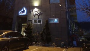 En byggnad med en skylt som visar texten ”GÄSTHUS” och en mindre skylt under som säger ”koreanskt kök”. En bil står parkerad framför byggnaden.