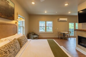 A hotel room with a bed, a seating area with a table and chairs, a fireplace, and a large window. - Haven Hotel (Boone)