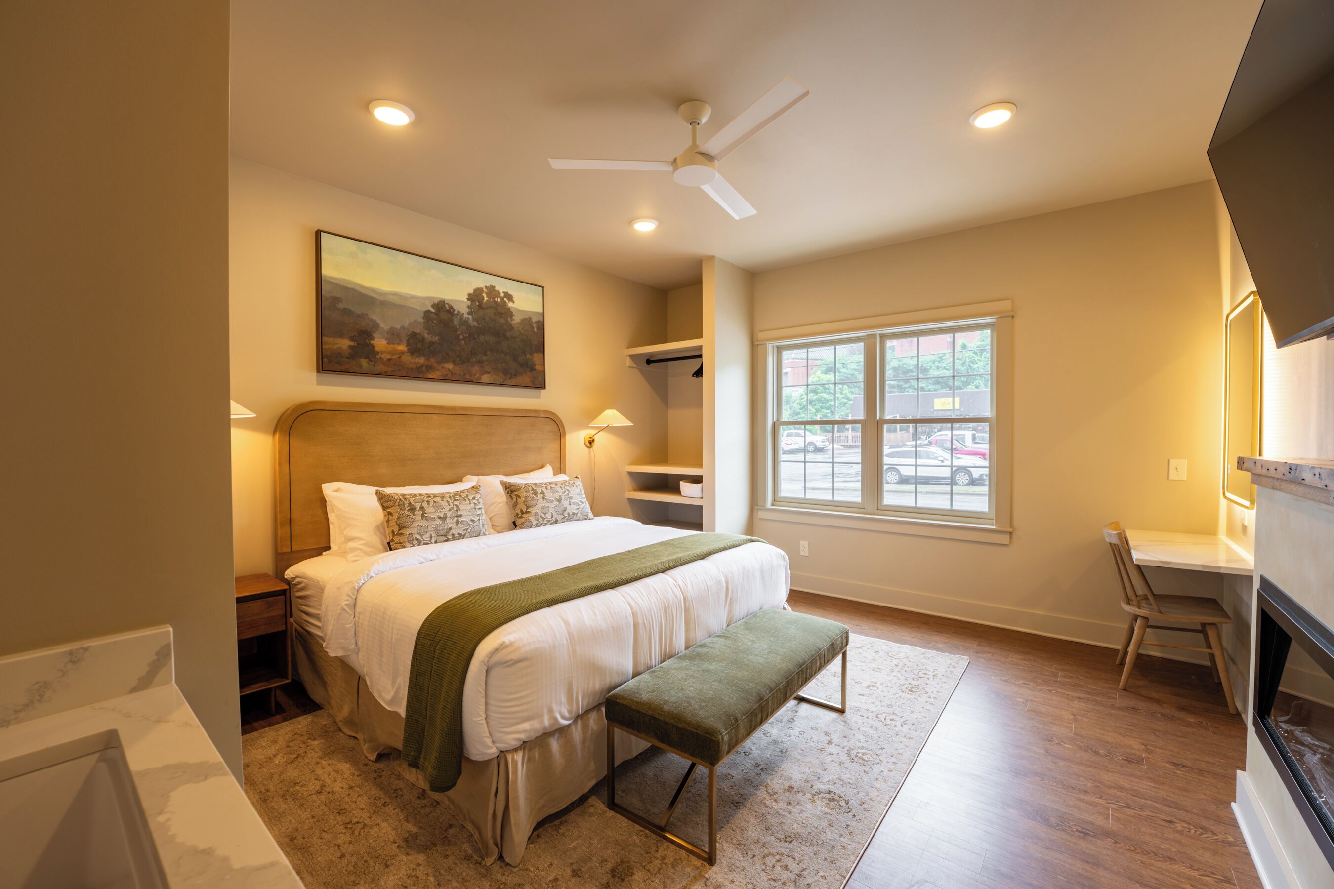 A bedroom with a bed, bedside tables, a desk, a chair, a window, and a ceiling fan.