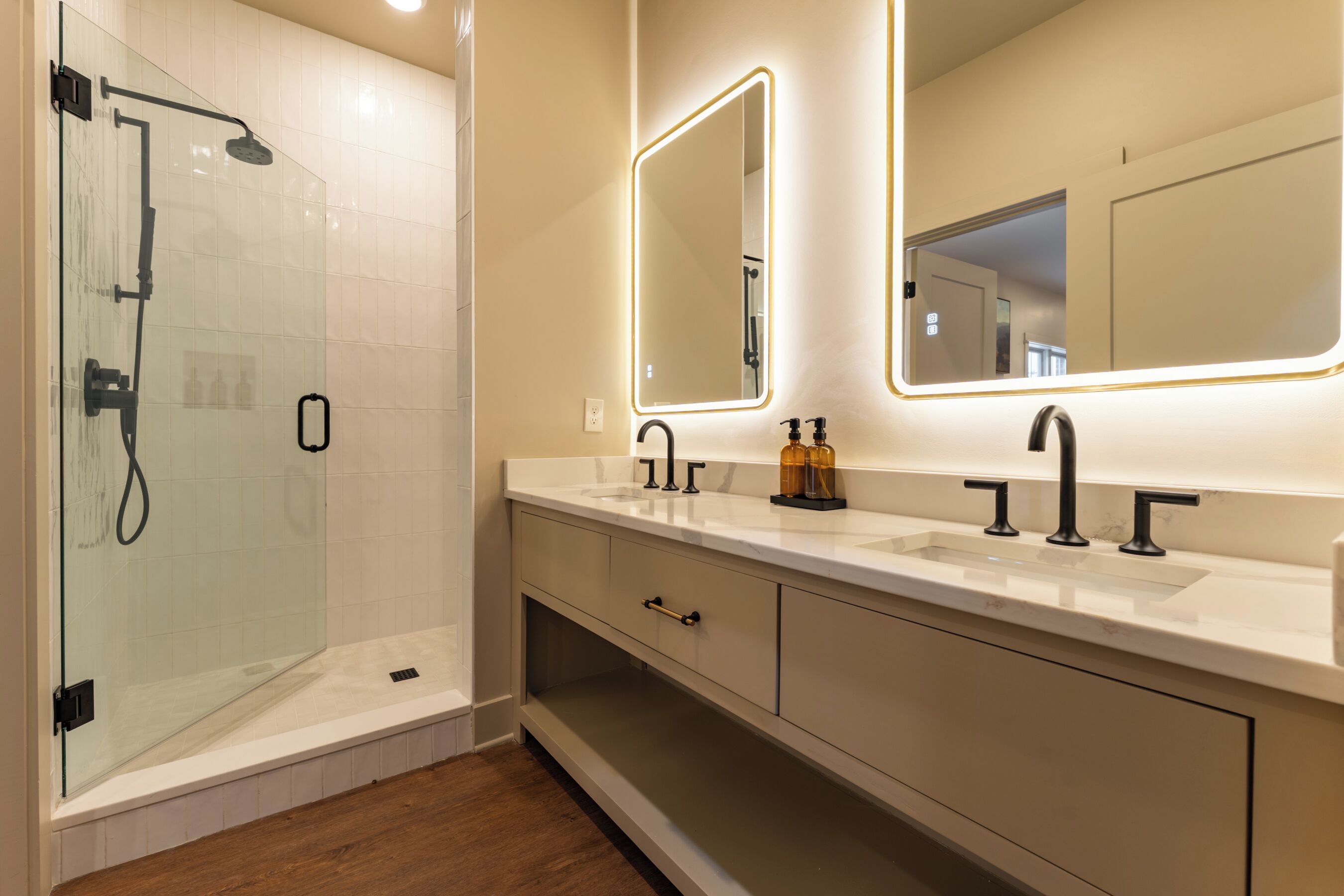 A modern bathroom with a glass shower enclosure, a vanity with a large mirror, and a sink with two faucets.
