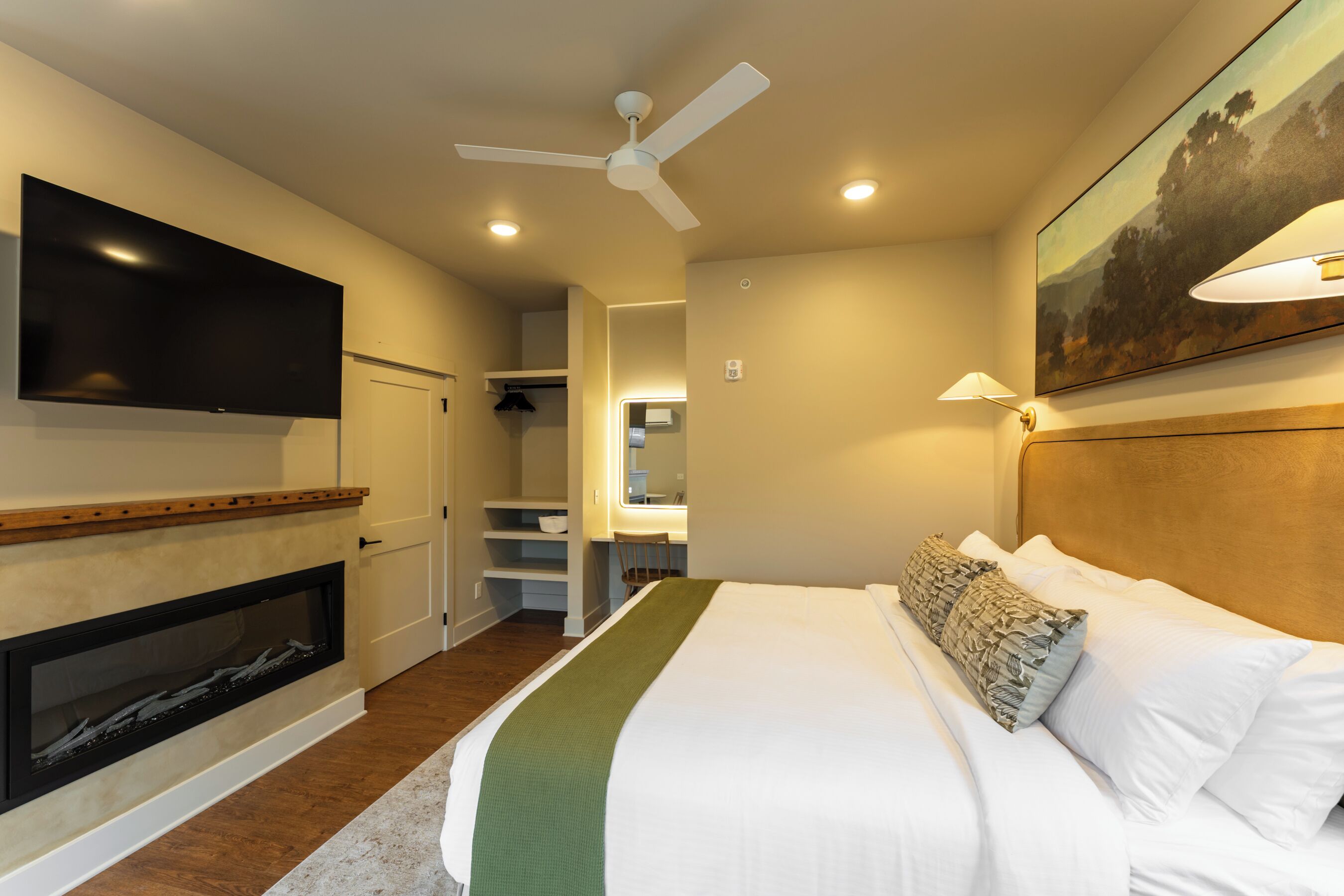 Una habitación de hotel con una cama, un televisor montado en la pared, un ventilador de techo y un cuadro colgado.