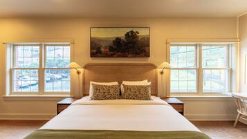 Une chambre à coucher avec un grand lit, deux tables de chevet, un tableau au-dessus du lit et des fenêtres de part et d’autre.