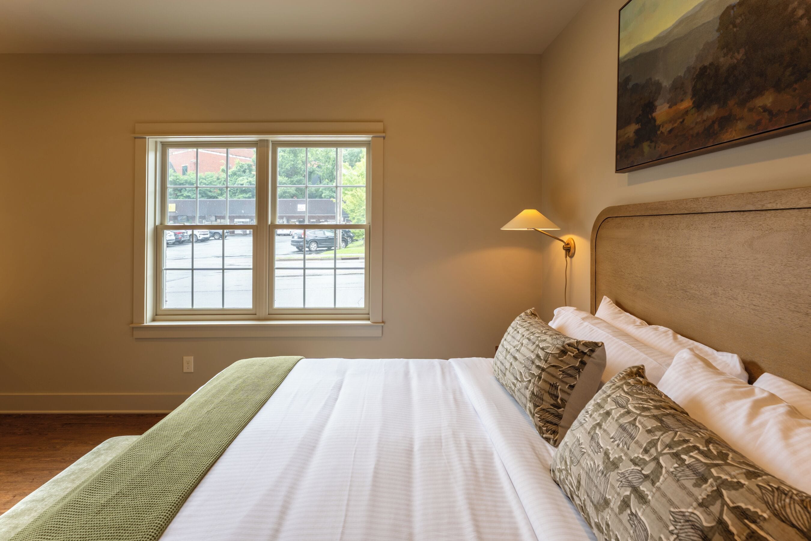 Quarto de hotel com uma cama grande, janela com vista para um estacionamento e um quadro na parede.