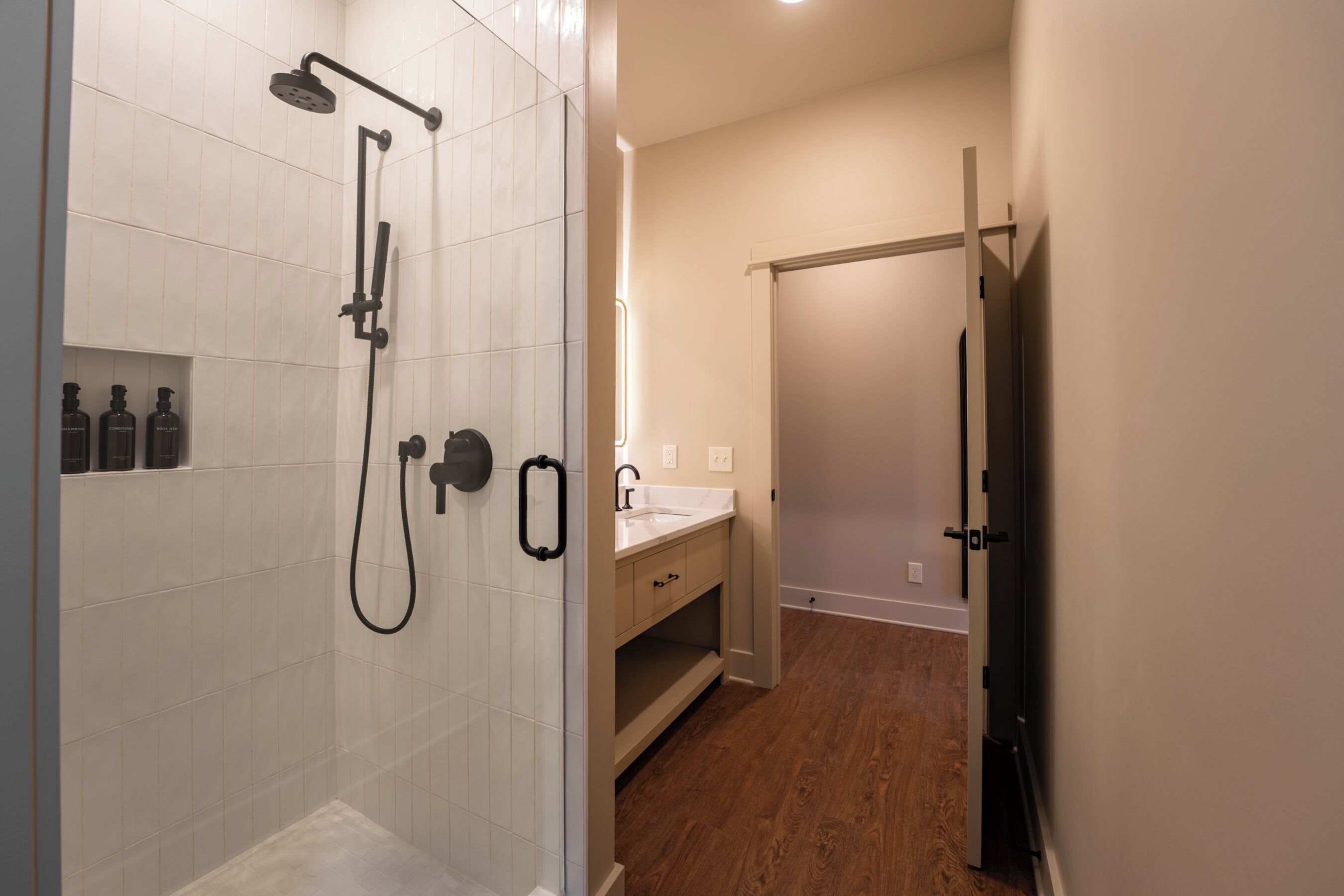 A modern bathroom with a walk-in shower, a vanity with a mirror, and a wooden floor.