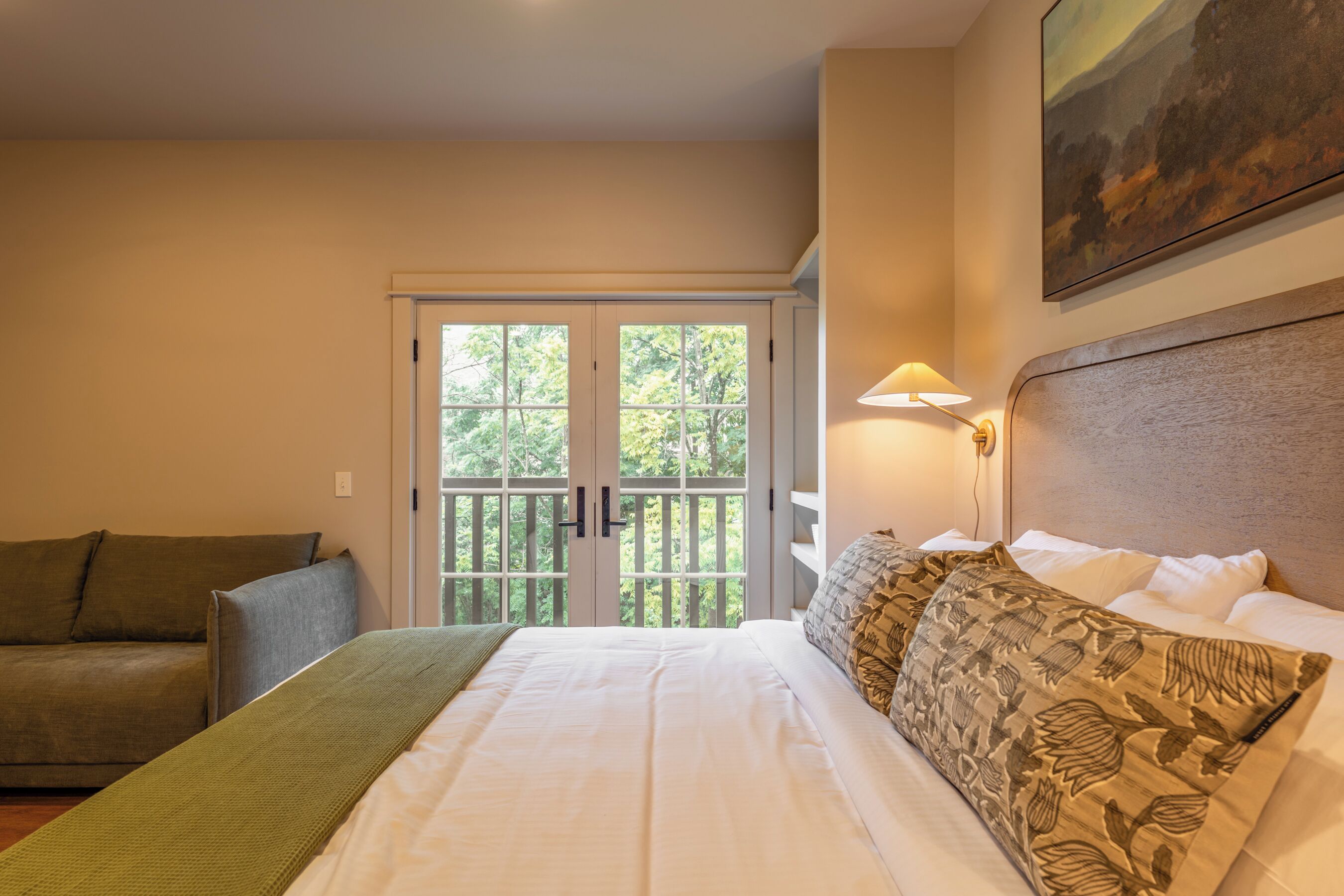 Una habitación de hotel con una cama, un sofá, un cuadro y vistas a través de una puerta.