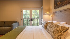 Une chambre d’hôtel avec un lit, un canapé, un tableau et une vue sur l’extérieur, visible à travers une porte.