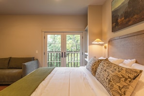 A hotel room with a bed, a sofa, a painting, and a view through a door. - Haven Hotel (Boone)