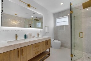 A modern bathroom with a large mirror, dual sinks, a glass shower enclosure, and a marble countertop. - Beautiful 4-bedroom Home in Prime Location (Hollywood)