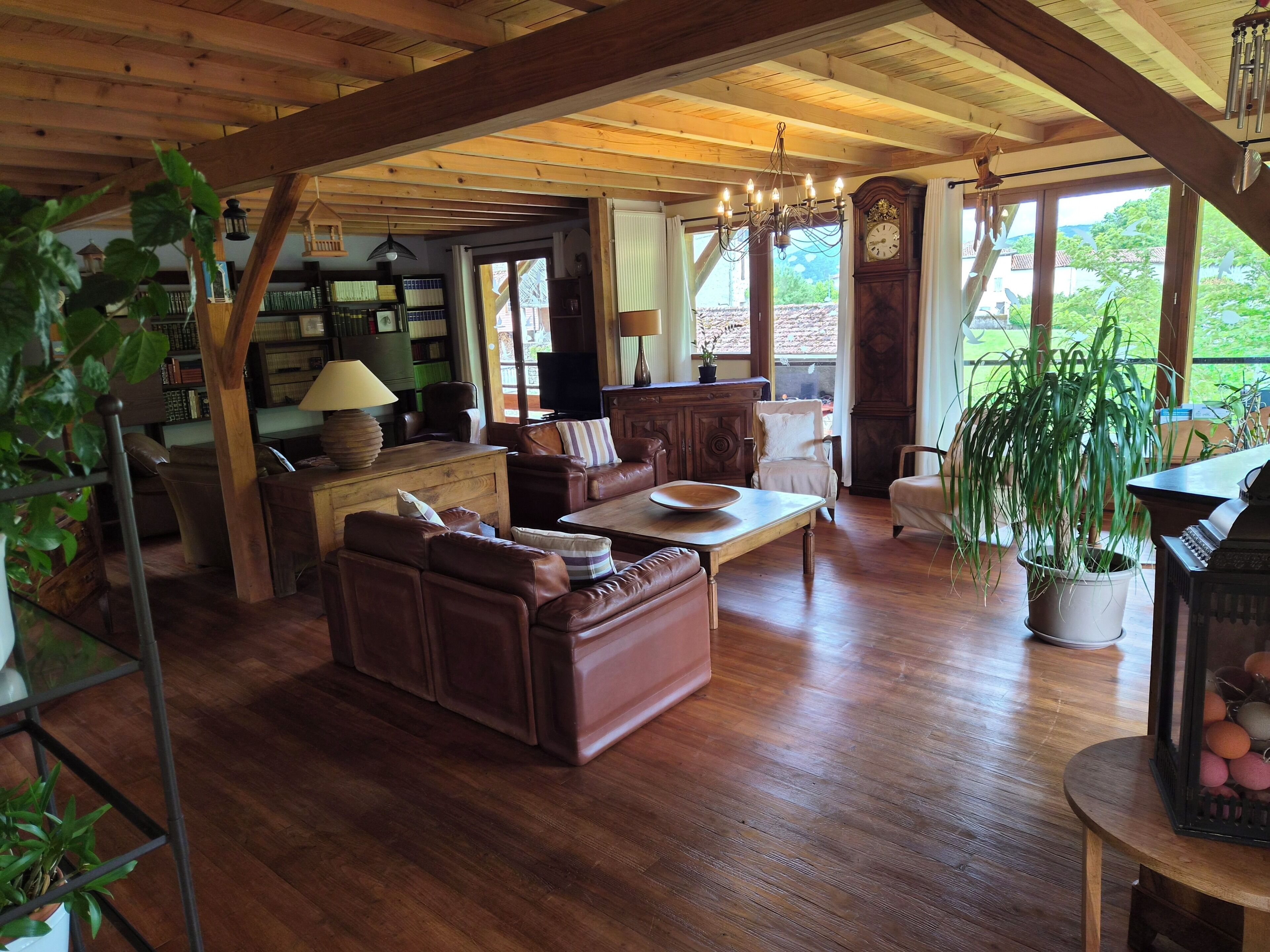 A cozy living room with wooden flooring, leather furniture, a piano, and a large window offering a view of the outdoors.