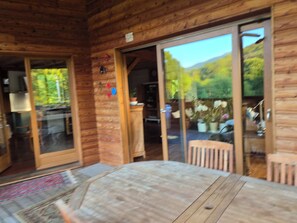 Interior de uma cabana de madeira com área de jantar, uma porta de vidro deslizante que dá para o exterior e uma cozinha visível.