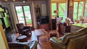 A cozy living room with leather furniture, a television, and a view of greenery outside. - Gîte Le Rucan Atypical house in the Pyrenees Commingeoises (Montastruc-de-Salies)