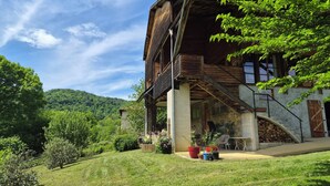 A rustic wooden house with a stone foundation, a covered porch, and a hillside view. - Gîte Le Rucan Atypical house in the Pyrenees Commingeoises (Montastruc-de-Salies)