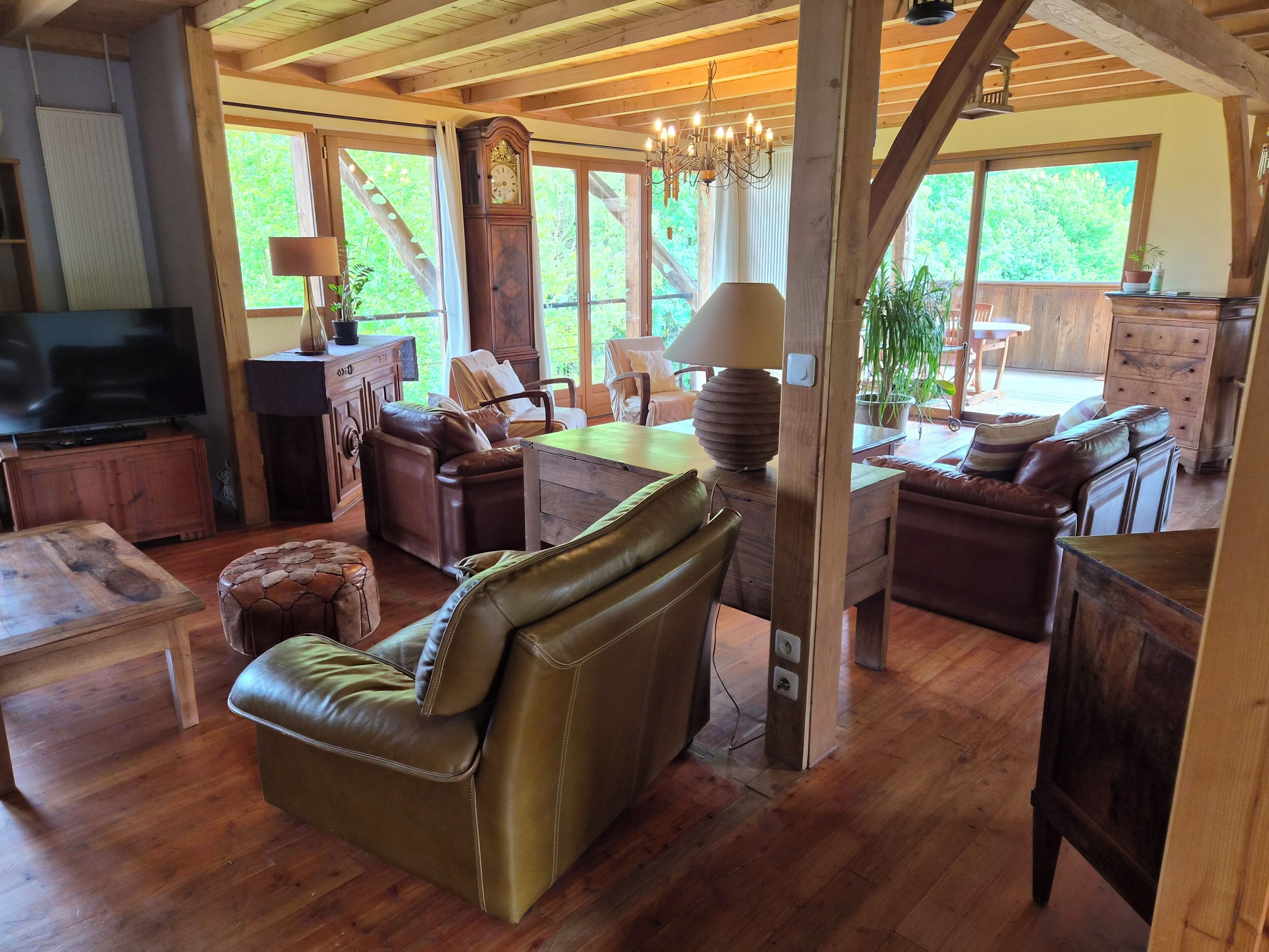 A spacious living area with a wooden ceiling, leather furniture, a large clock, and a chandelier.