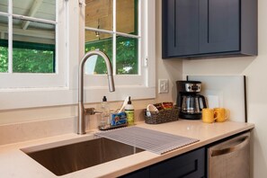 A kitchen with a stainless steel sink, a coffee maker, and a window with a view of greenery.