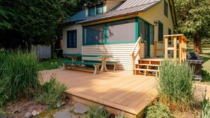 Una piccola baita con una veranda in legno, una panca e un'area barbecue.