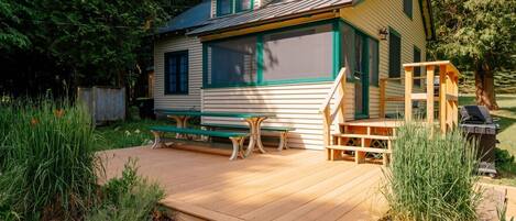 A small cabin with a wooden deck, a bench, and a grill area.