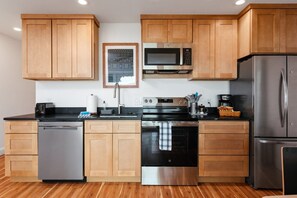 A modern kitchen with wooden cabinets, stainless steel appliances, a microwave, a dishwasher, and a refrigerator.