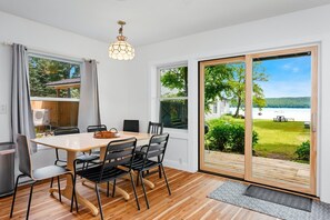 Ein Essbereich mit Tisch und Stühlen, einer Pendelleuchte und Seeblick durch große Fenster.