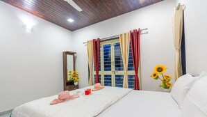 Un dormitorio con cama, una ventana con cortinas, un espejo y un florero con flores.