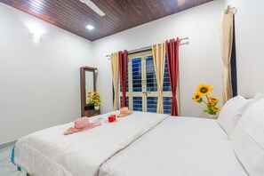 A bedroom with a bed, a window with curtains, a mirror, and a vase with flowers. - Sun Set Villa (Mawal)