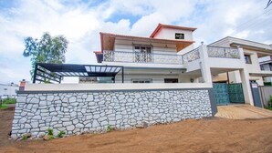 Una casa a due piani con un muro in pietra, un balcone con ringhiere ornamentali e un cartello con la scritta 'SUNRISE'.