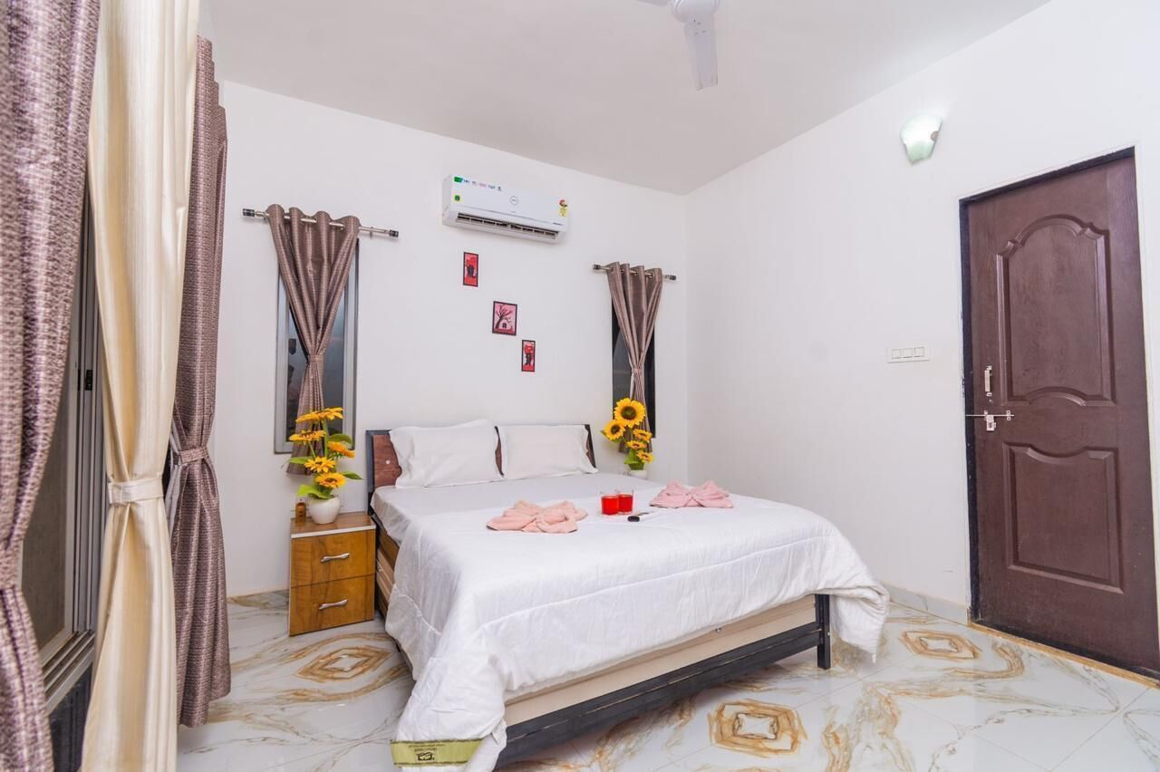 A bedroom with a bed, curtains, an air conditioning unit, a wooden cabinet, and a door.