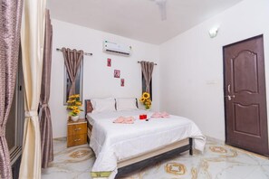 Un dormitorio con cama, cortinas, aire acondicionado, un armario de madera y una puerta.