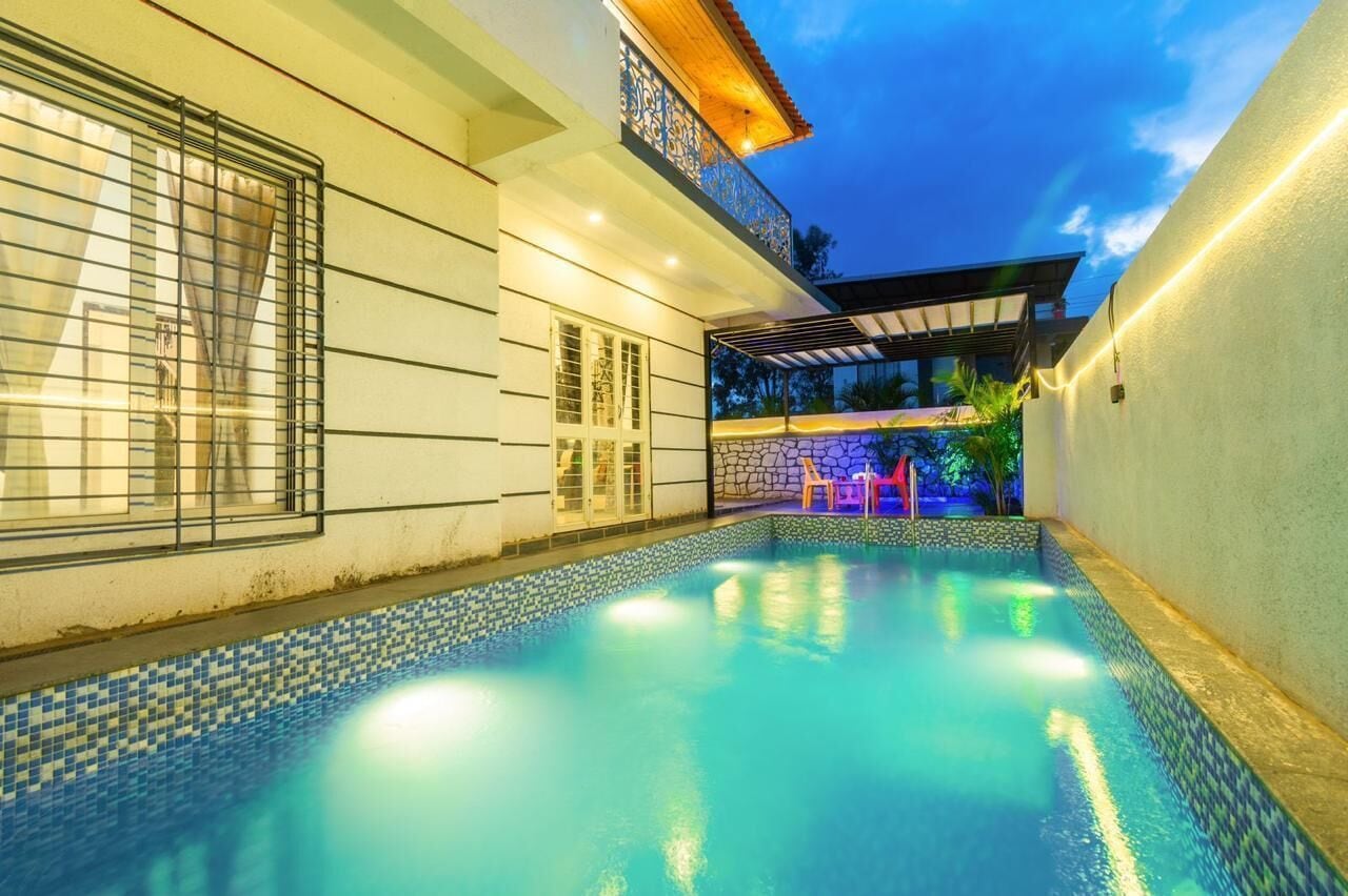 A swimming pool with a tiled edge, a covered outdoor seating area, and a building with a balcony.