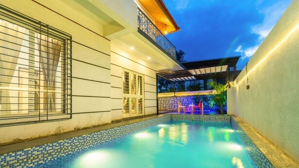 Una piscina con bordo piastrellato, una zona relax all'aperto coperta e un edificio con un balcone.