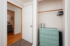 A hallway leading to a room with a white door, a wooden floor, and a teal dresser with drawers.