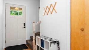 Un pasillo con una puerta blanca, una escalera de madera y un tendedero fijado a la pared.