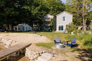 A beachside property with a wooden dock, a sandy area, and a small house with a balcony. - Camp Haven | Sandpiper Cottage | 4BR Beachfront | Glen Lake (Empire)