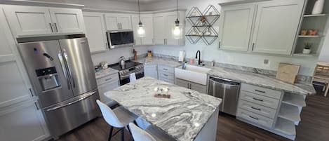 A modern kitchen with stainless steel appliances, a marble island, and a built-in dishwasher.