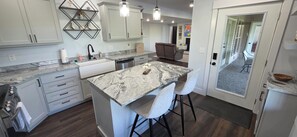 A modern kitchen with a central island, bar stools, and a dining area with a sofa. - Cozy apartment in the country (West Branch)