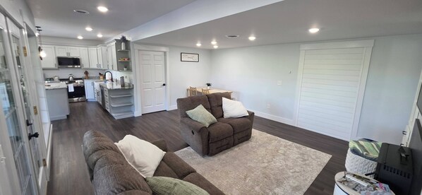 A spacious living area with a brown sofa, a dining table, and a kitchen in the background.