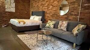 Ein Schlafzimmer mit einem Bett, einem Schlafsofa, einem runden Tisch und einem Spiegel an einer Ziegelwand.