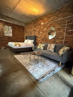 Ein Schlafzimmer mit einem Bett, einem Schlafsofa, einem runden Tisch und einem Spiegel an einer Ziegelwand.